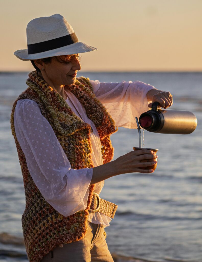 Adult woman pouring yerba mate drink at sunset on a Montevideo beach, Uruguay.
